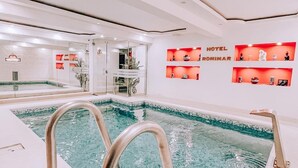 Une piscine à l’eau claire, entourée de murs blancs et dotée d’un plafond avec des luminaires encastrés.