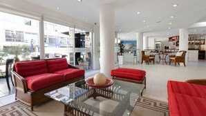 Un hall d’hôtel spacieux, avec un canapé rouge, une table basse en verre et un coin repas doté de chaises en bois.