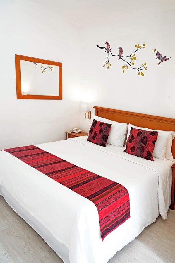 Una cama bien hecha con un edredón blanco y rojo a rayas, un cabecero de madera y dos almohadas a juego.