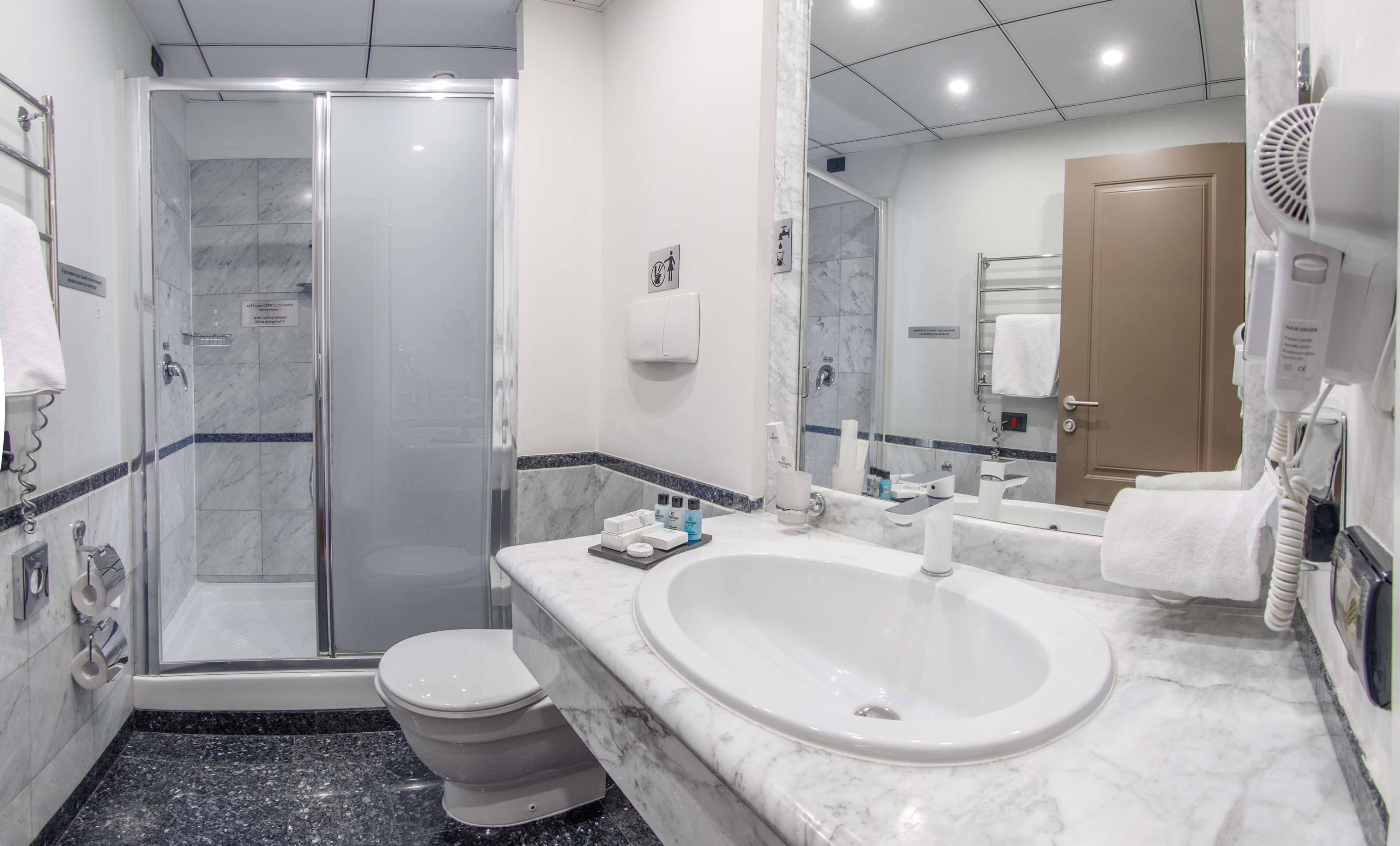 A modern bathroom with a glass-enclosed shower, a white sink with a marble countertop, and a toilet.