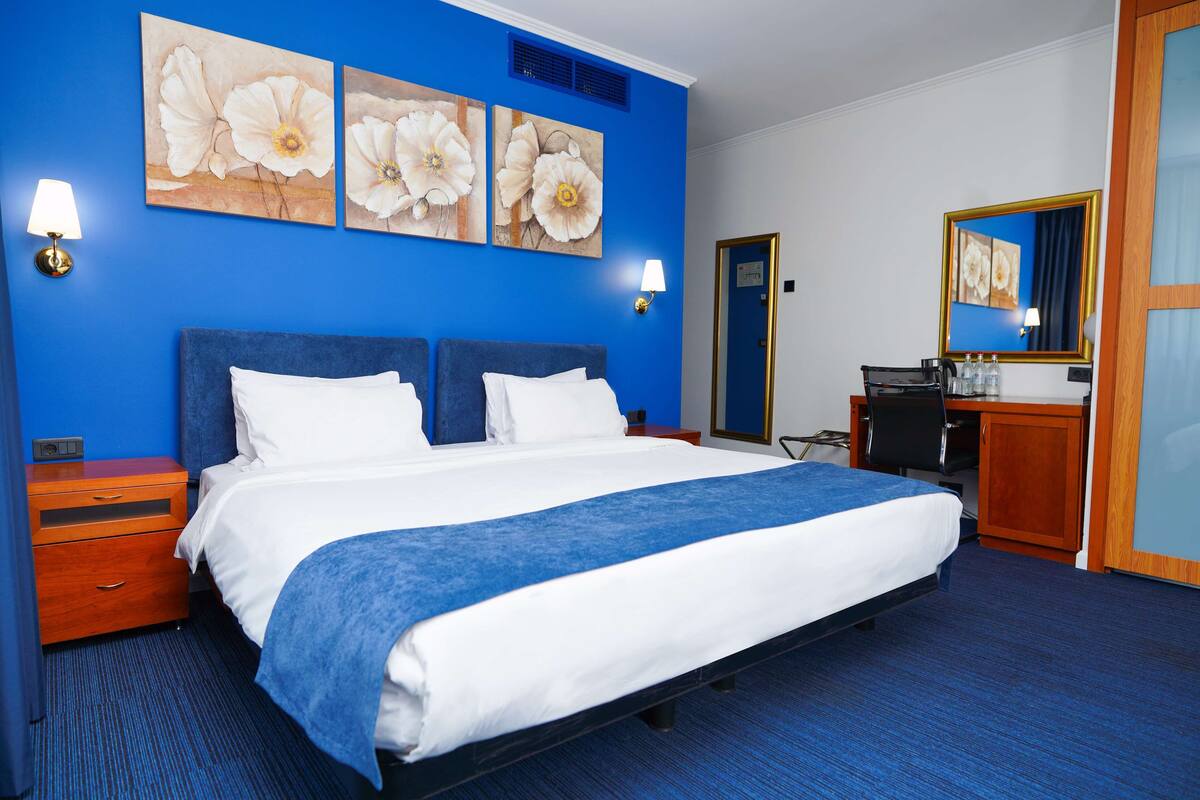 A hotel room with a large bed, two wall-mounted lamps, and three floral paintings.