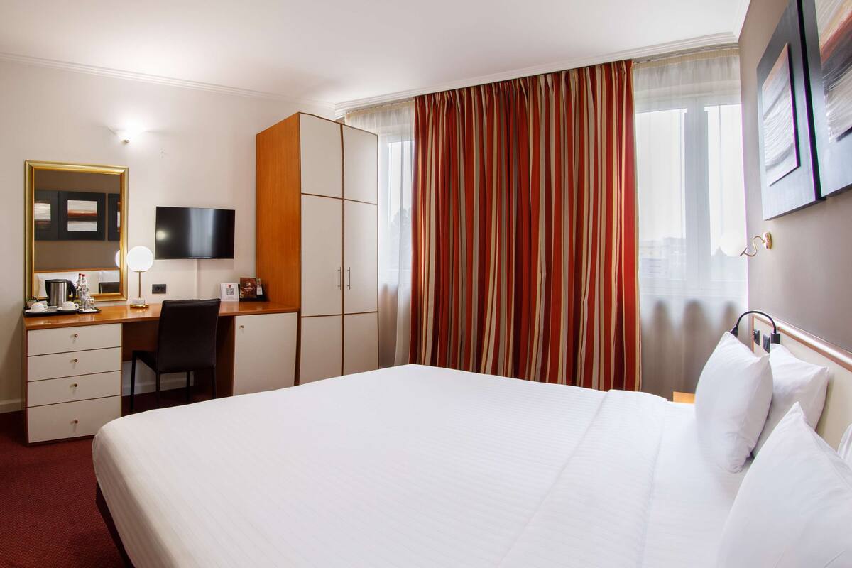 A hotel room with a bed, a desk with a chair, a television, and a wardrobe.