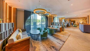 En moderne hotellobby med et siddeområde, store vinduer og en receptionsdisk.