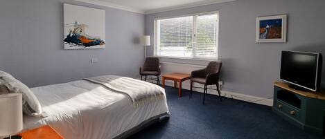 A hotel room with a bed, a desk, a chair, a TV, and artwork on the walls.