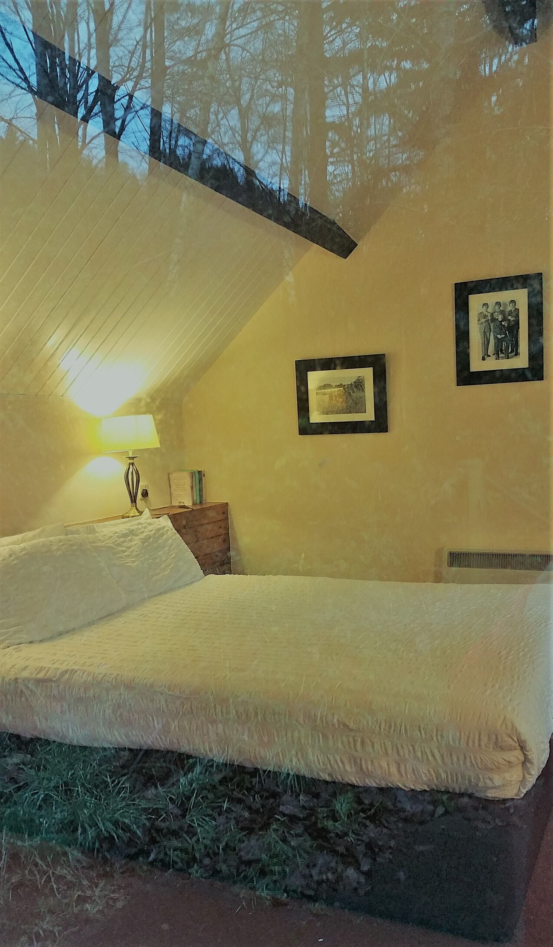 Un dormitorio con una cama, una mesita de noche, una lámpara y cuadros en la pared.