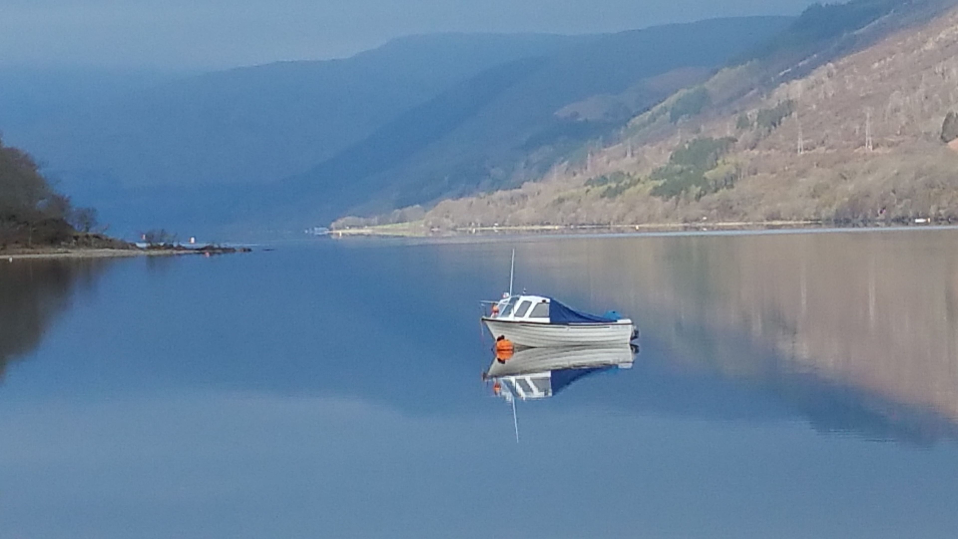 A calm lake with a small boat anchored in the center, surrounded by hills and a clear sky.