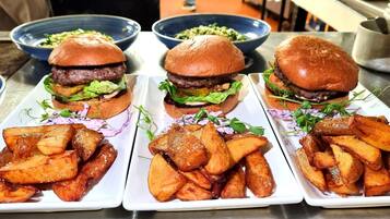 Tres hamburguesas con papas fritas en platos blancos, cada una acompañada de una ensalada en un tazón azul.