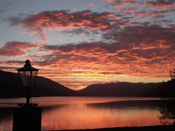 A sunset over a calm lake with mountains in the background and a street lamp in the foreground.