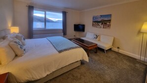 Habitación de hotel con cama, sofá, televisor y un cuadro de una playa.