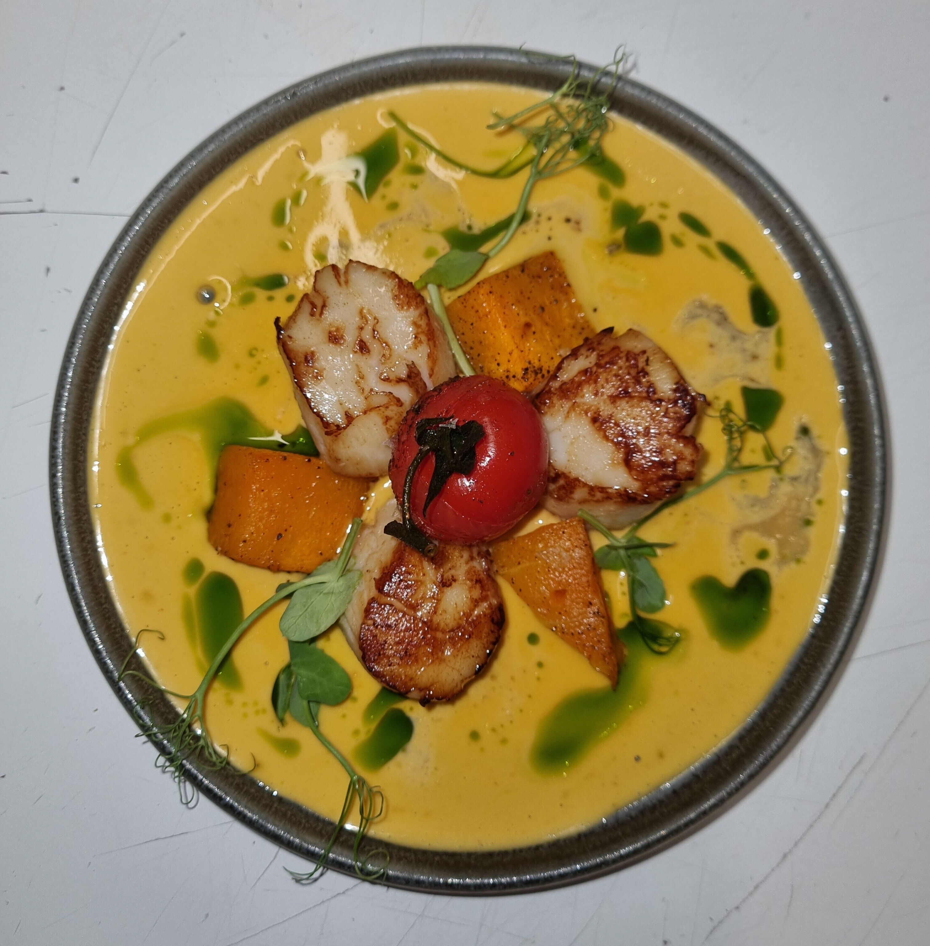 A plate of food with seared scallops, a tomato, and vegetables in a creamy sauce.
