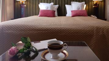 Habitación de hotel con una cama bien hecha, una mesita de noche con una taza de café, una rosa y una lámpara.