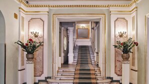A grand staircase with a black and gold carpet leading to a room with a large mirror and a chandelier. - Grand Hotel (Kraków)