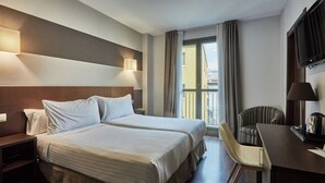 A hotel room with two beds, a desk, a chair, a TV, and a window with curtains. - Silken Sirimiri (Bilbao)