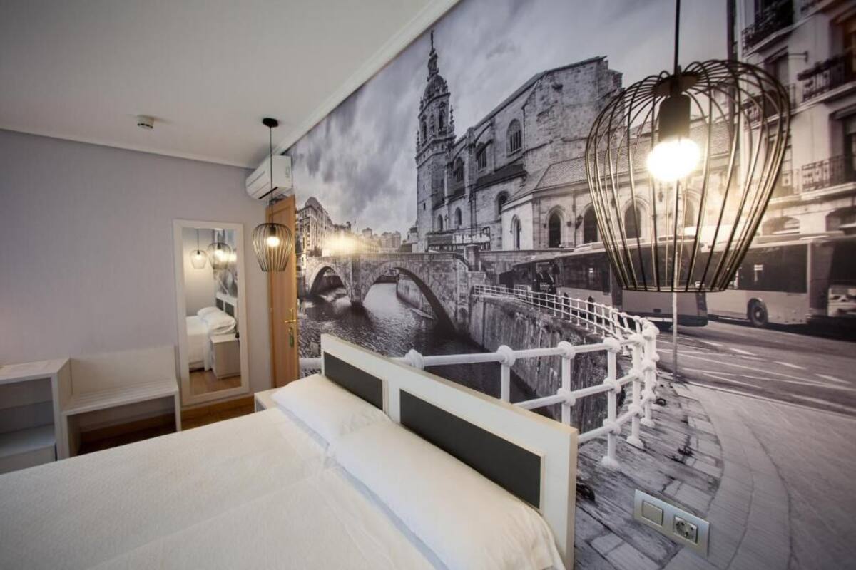 A bedroom with a large cityscape mural, a bed, bedside tables, and hanging pendant lights.