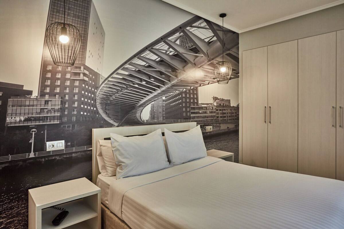 A hotel room with a bed, nightstands, a wardrobe, and a mural of a cityscape.