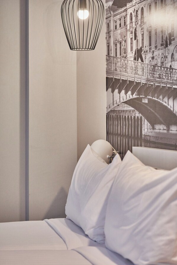 Una habitación de hotel con una cama, una lámpara fijada a la pared y un cuadro grande con un puente.