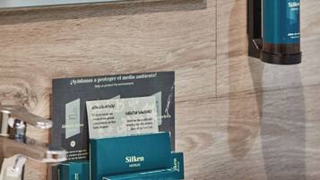 Un baño con espejo, lavamanos, dispensador de jabón y un cartel que promueve la protección del medio ambiente.