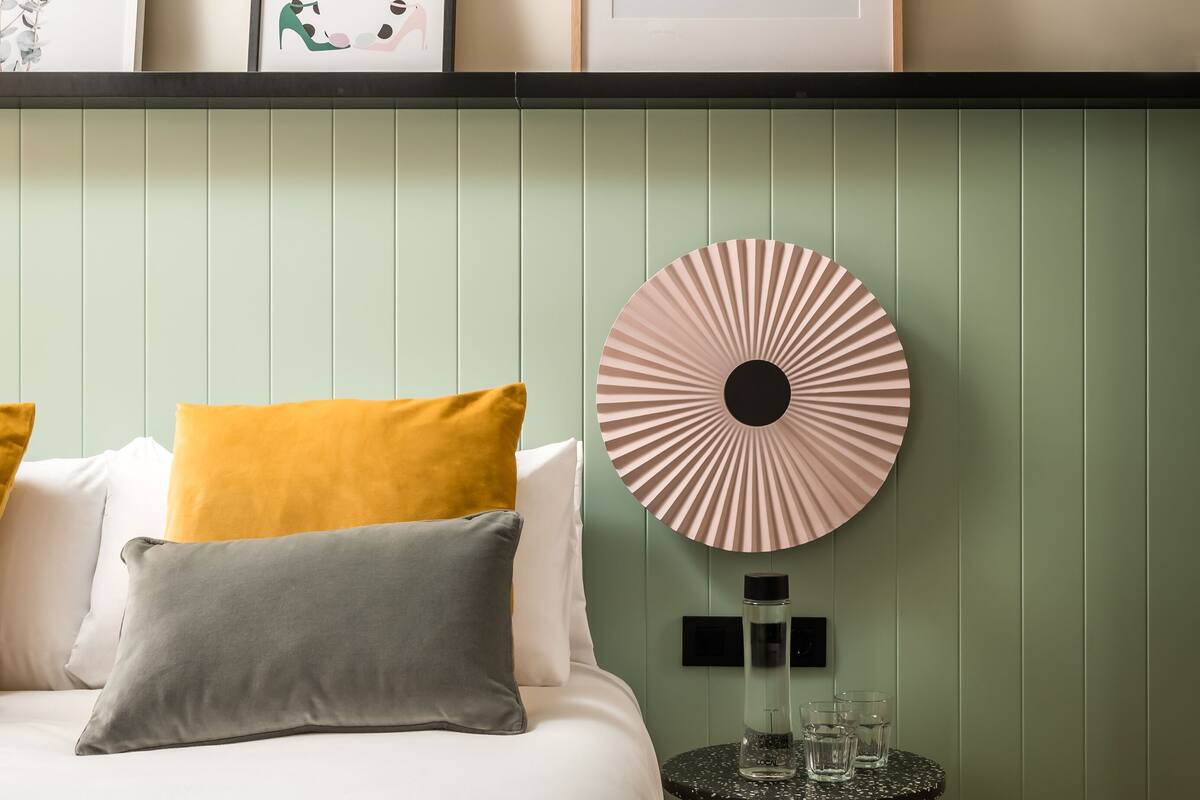 A neatly arranged bedroom with a bed, pillows, a bedside table with glasses, and a wall-mounted fan.