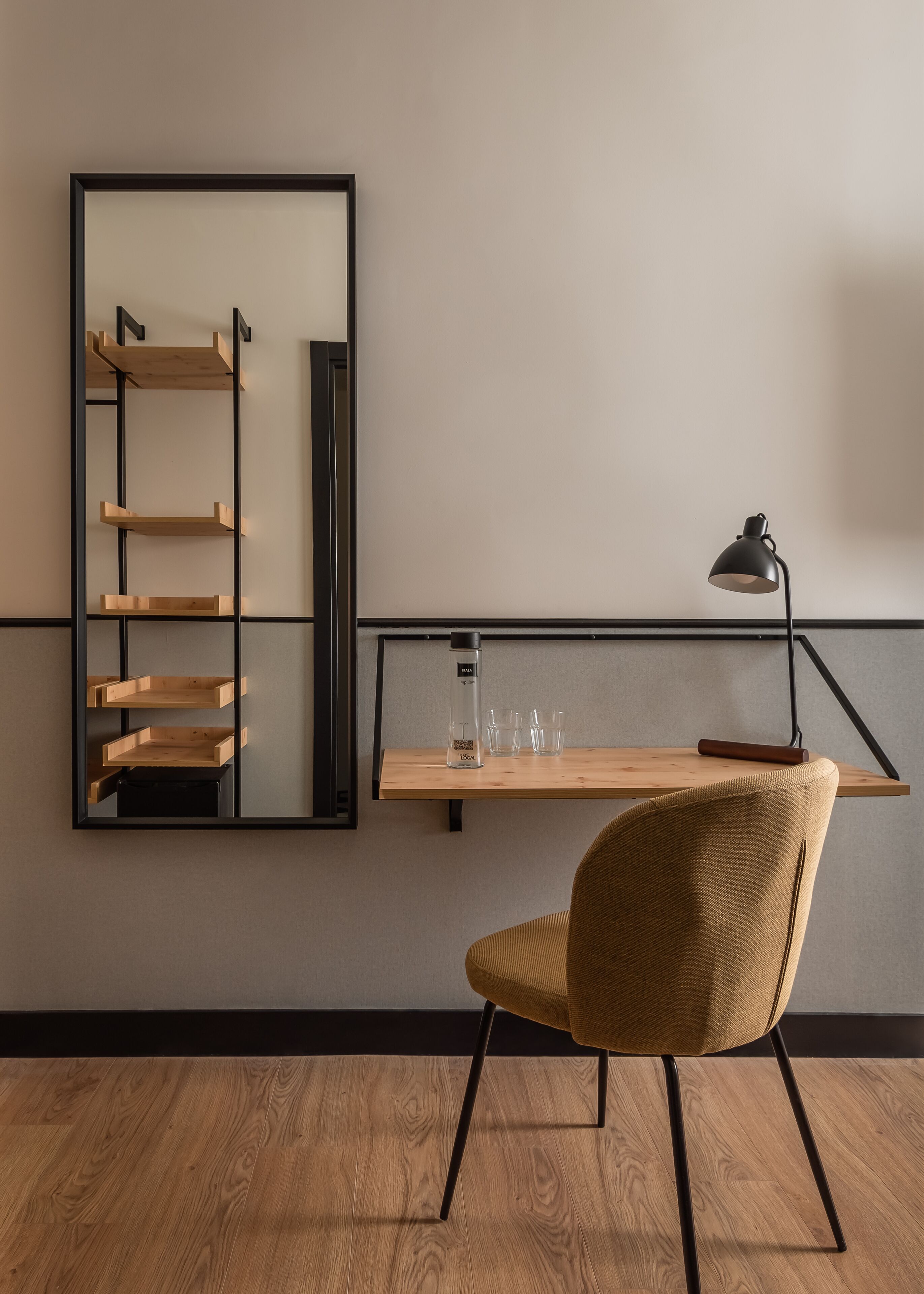 A modern room with a wooden floor, a chair, a desk with a lamp, a shelf with glasses, and a ladder.