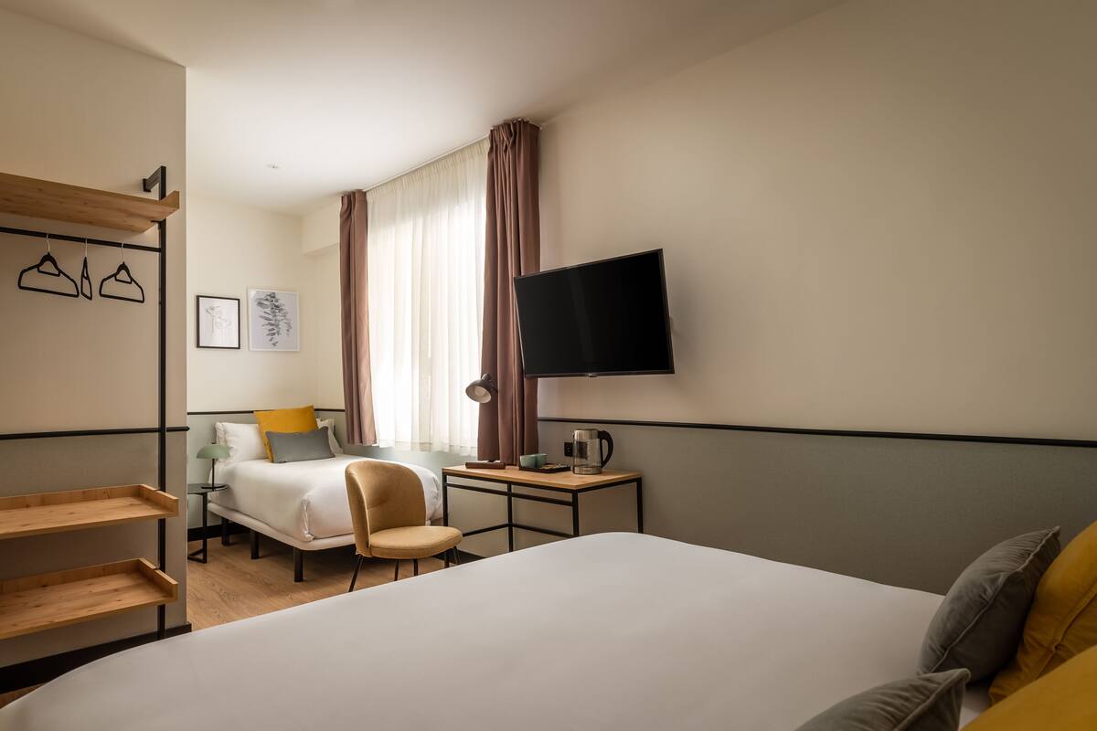 A hotel room with a large bed, a desk with a chair, a TV, and a window with curtains.