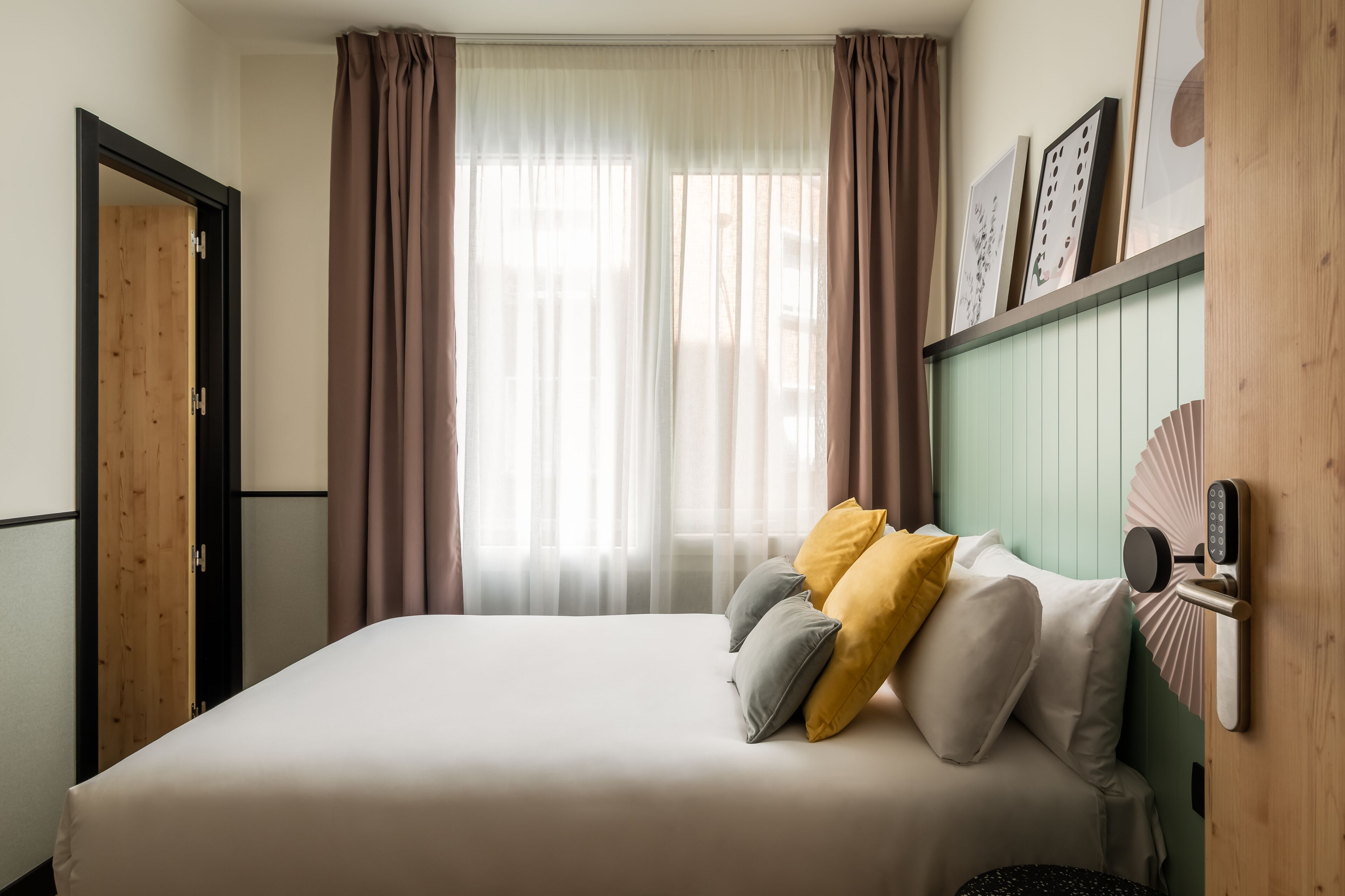 Een slaapkamer met een bed, gordijnen, een deur en een kunstwerk aan de muur.