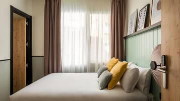 Een slaapkamer met een bed, gordijnen, een deur en een kunstwerk aan de muur.