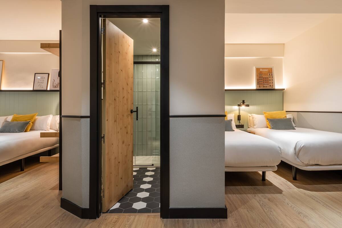 A modern hotel room with two beds, a wooden door, and a tiled shower area.