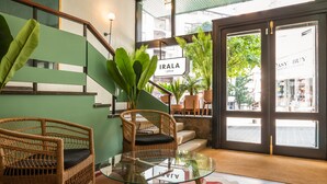 Un hall d’entrée avec des fauteuils en osier, une table en verre et un escalier aux panneaux verts.