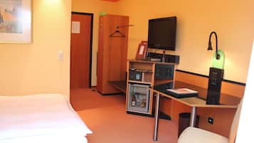 Habitación de hotel con cama, escritorio con computadora, televisión, refrigerador pequeño y una silla.