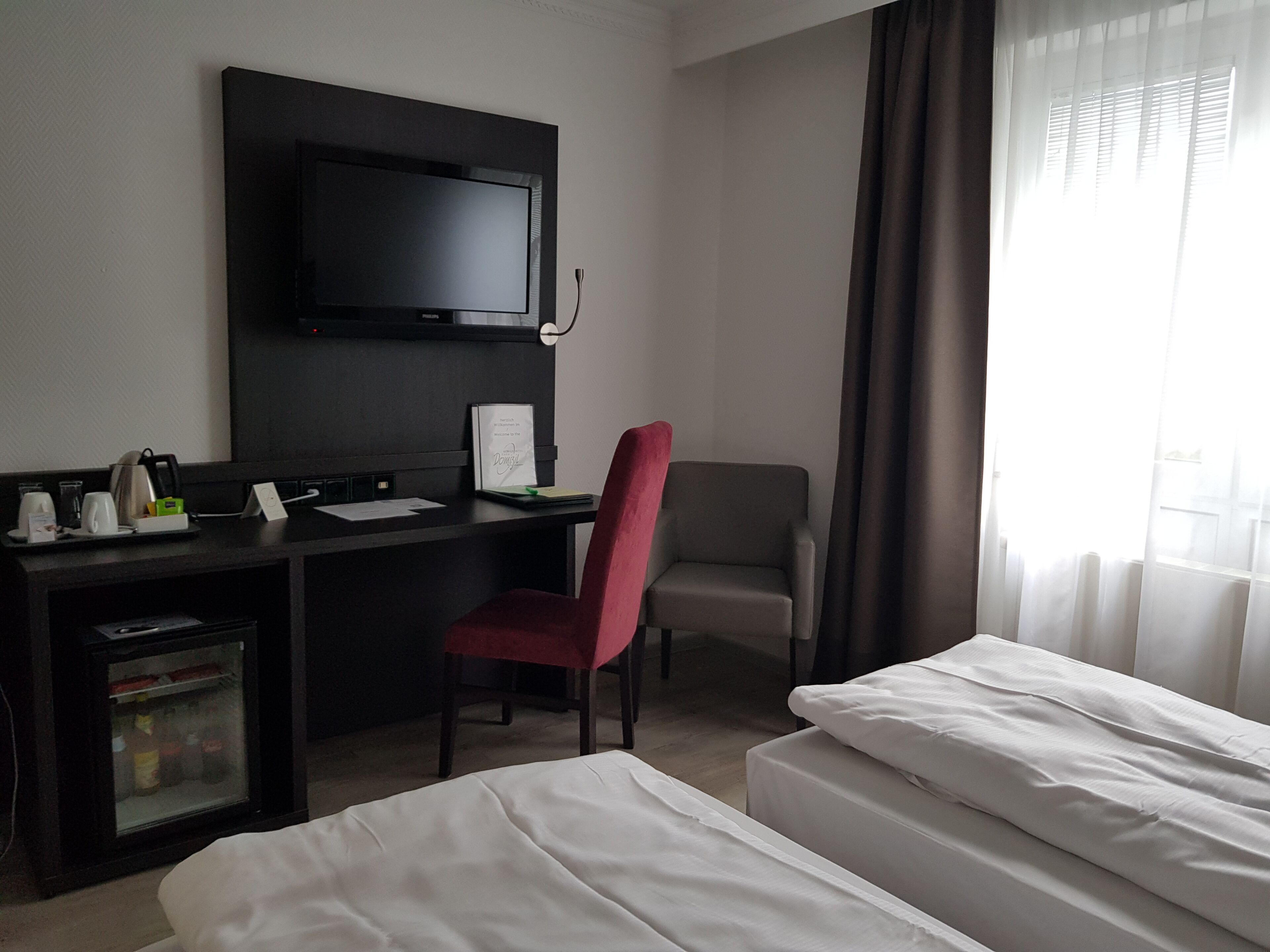 Een hotelkamer met een bed, een bureau met een computer, een stoel en een televisie aan de muur.