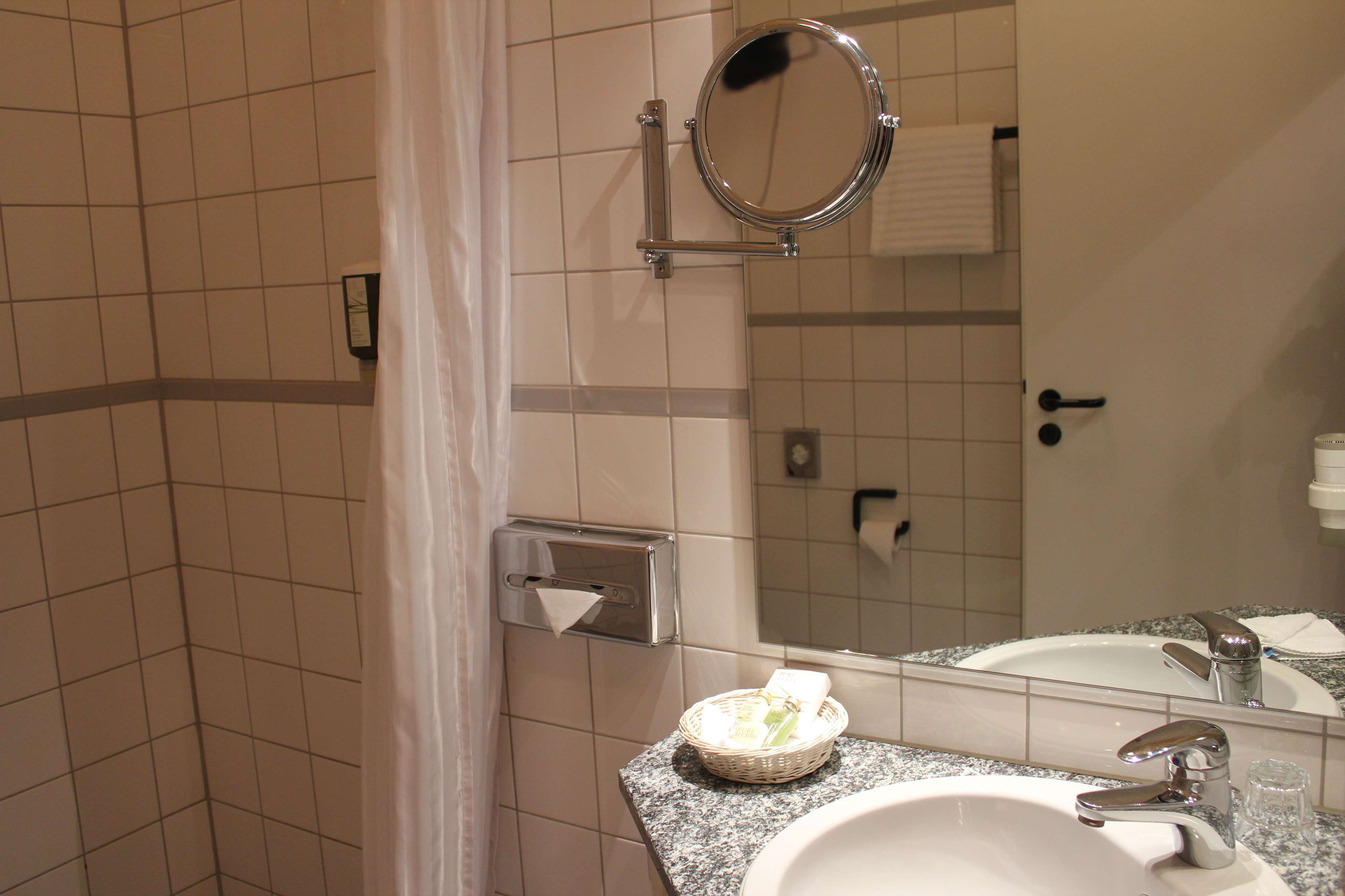 Un baño con lavamanos, espejo, dispensador de toallas y una cesta de artículos de aseo.
