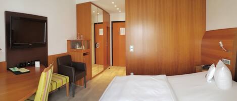 Una habitación de hotel con cama, escritorio con silla, televisor y armario.