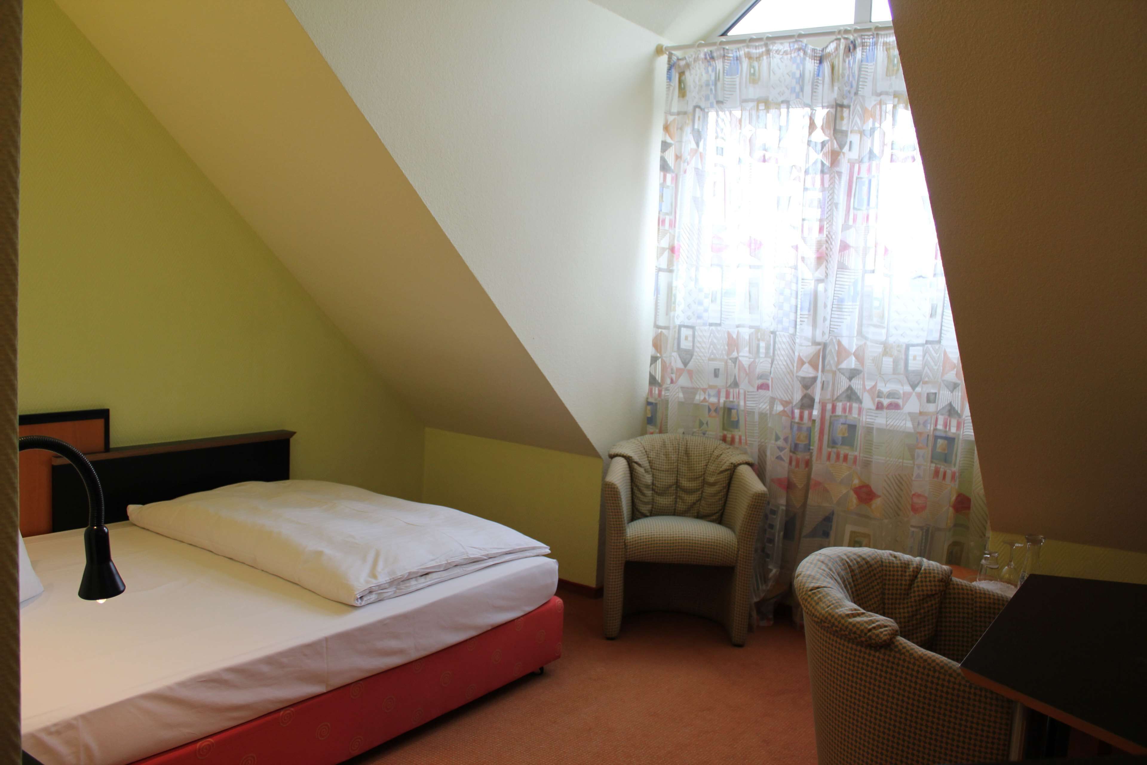 Una habitación pequeña y triangular con una cama, una silla y una mesa.