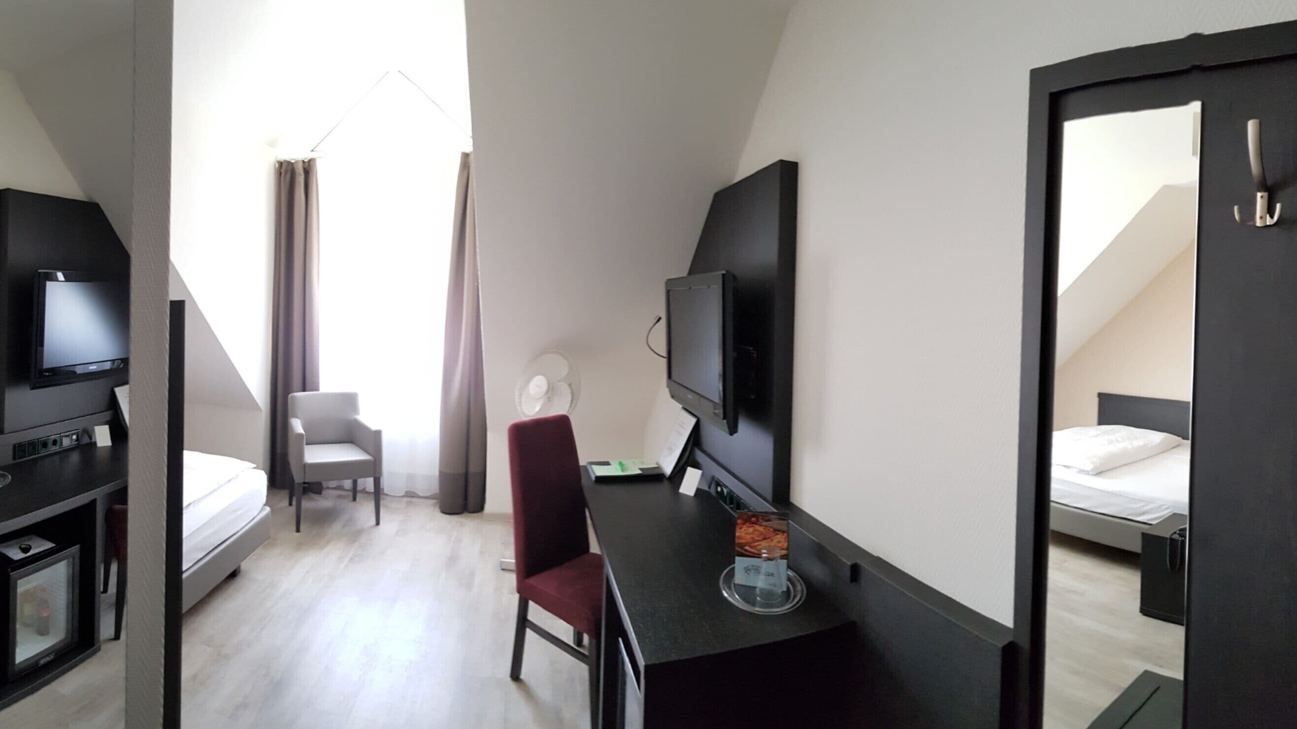 Ett hotellrum med en säng, ett skrivbord med en tv, en stol och ett fönster med gardiner.
