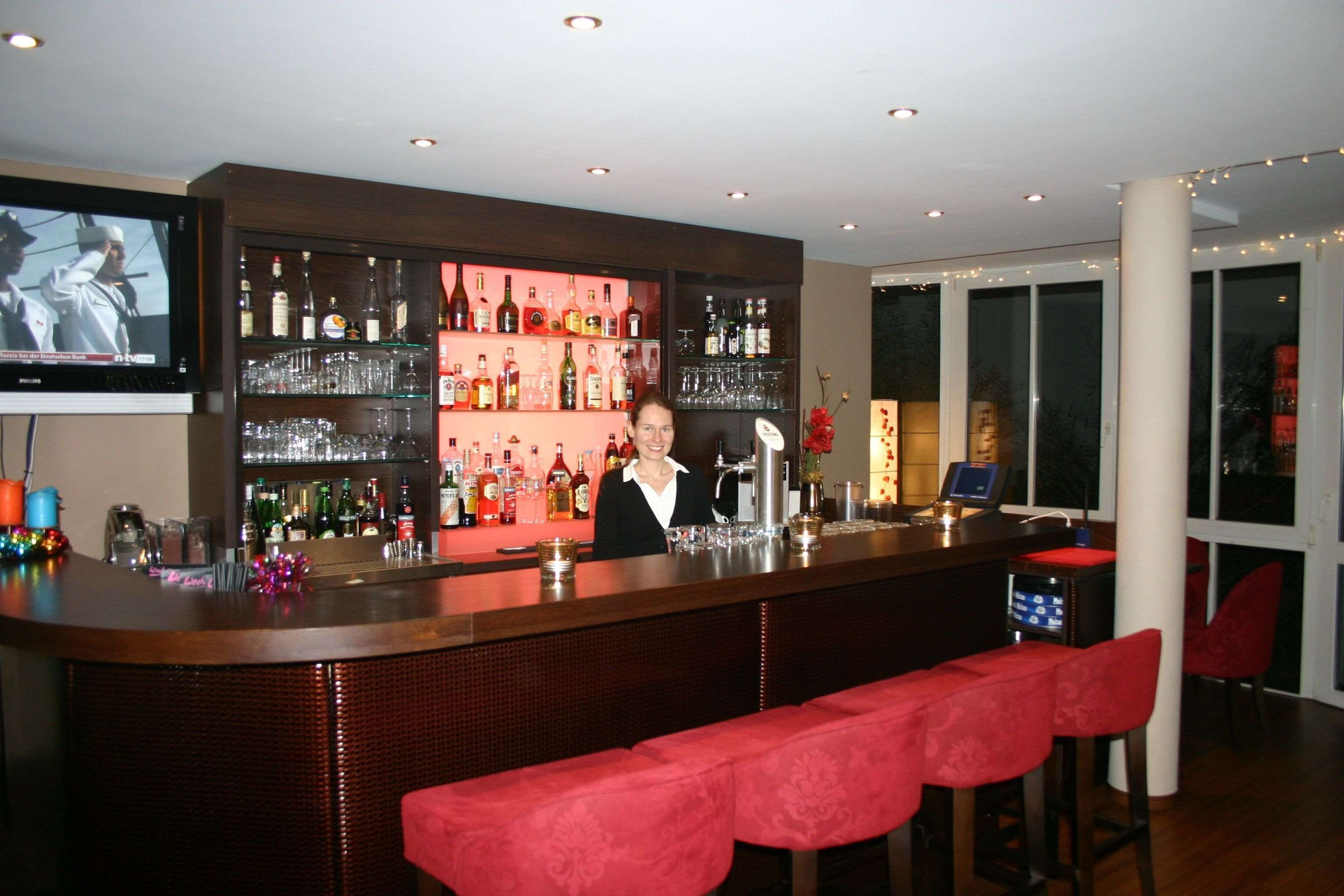 A bar area with a bartender, shelves of liquor bottles, glasses, and a television screen.