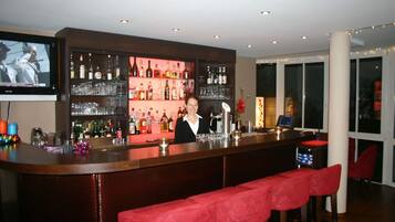 A bar area with a bartender, shelves of liquor bottles, glasses, and a television screen.