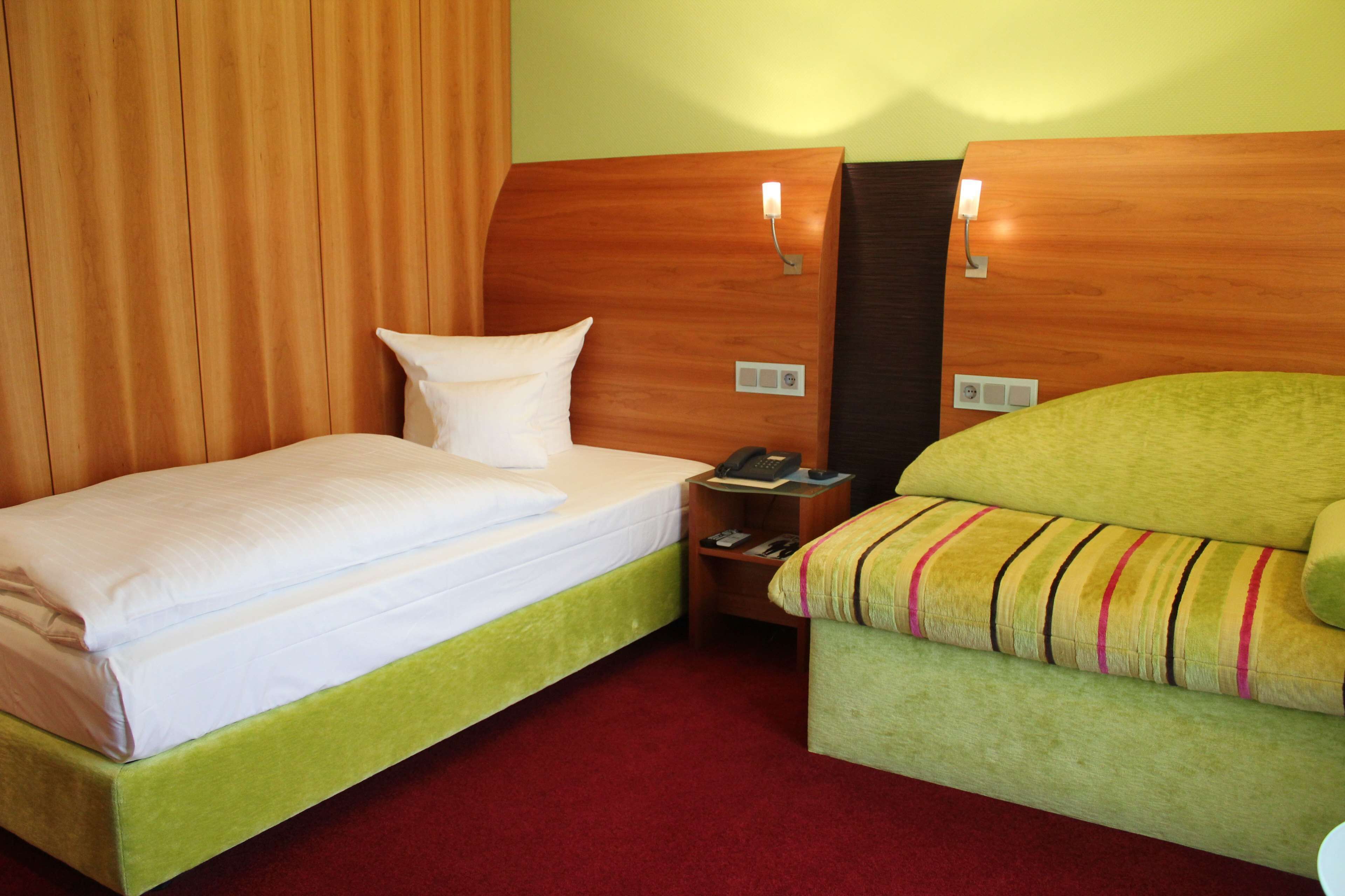 A hotel room with a bed, a green sofa, a nightstand with a phone, and a wooden headboard.