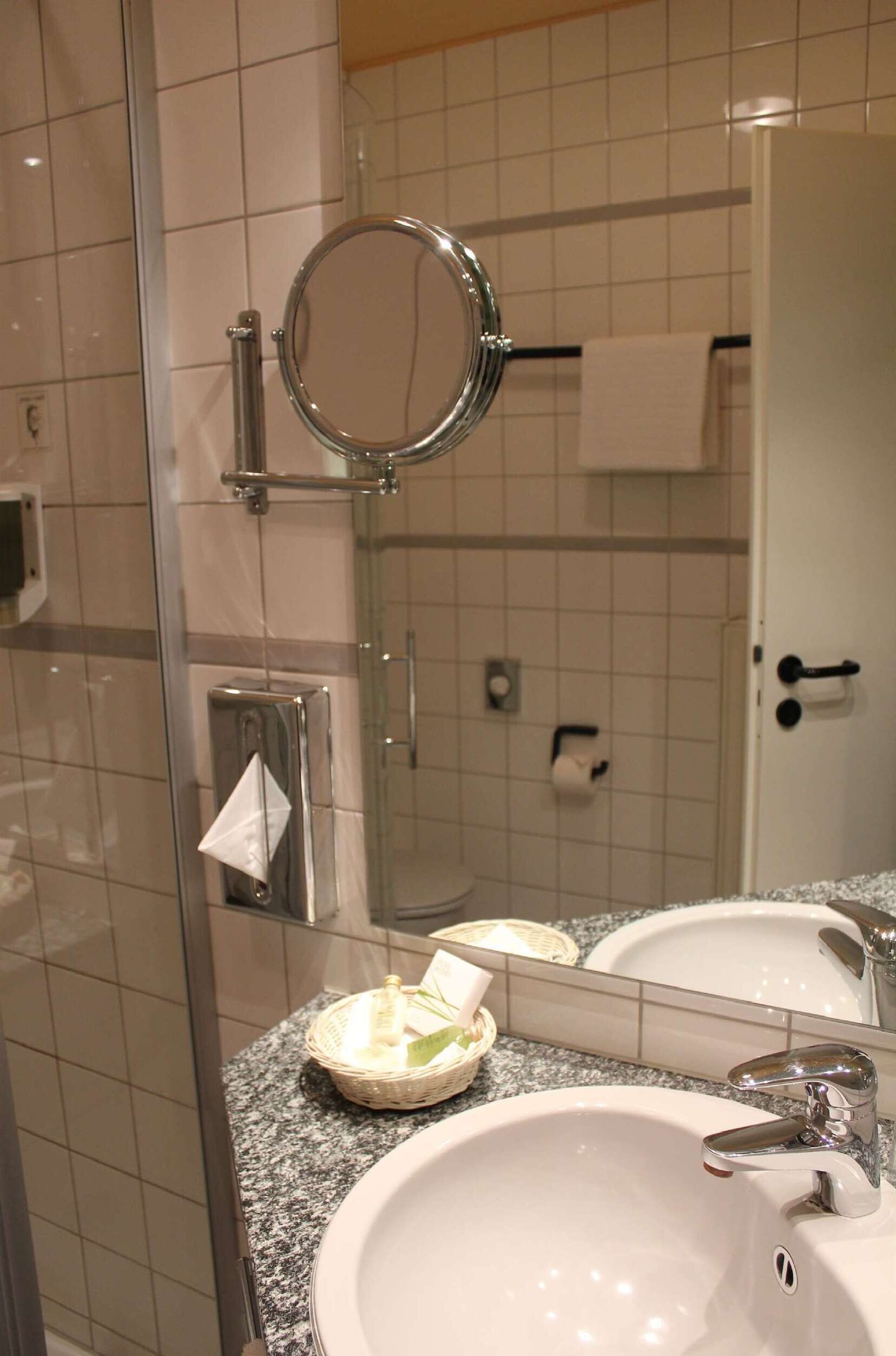 Une salle de bain avec une douche à parois de verre, un miroir rond, un lavabo blanc avec un robinet chromé et un porte-serviettes.