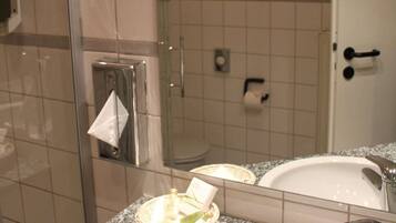 Une salle de bain avec une douche à parois de verre, un miroir rond, un lavabo blanc avec un robinet chromé et un porte-serviettes.