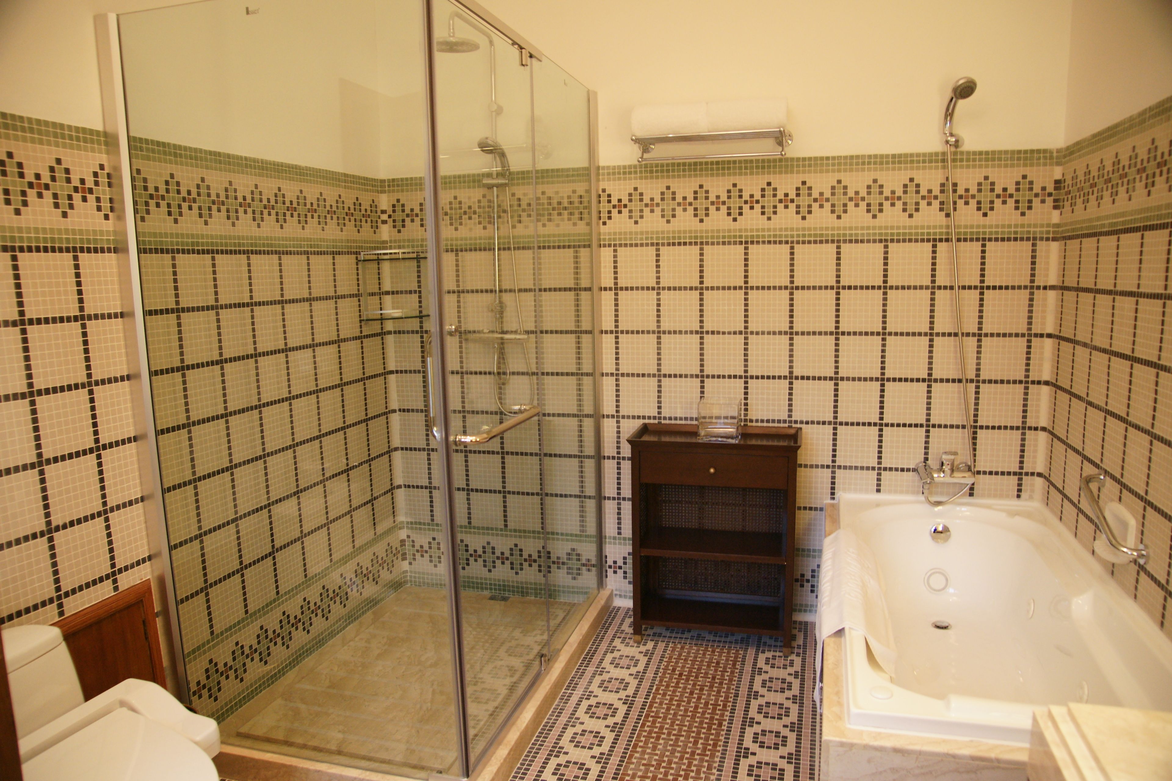 A bathroom with a glass shower enclosure, a bathtub, and mosaic tile walls.