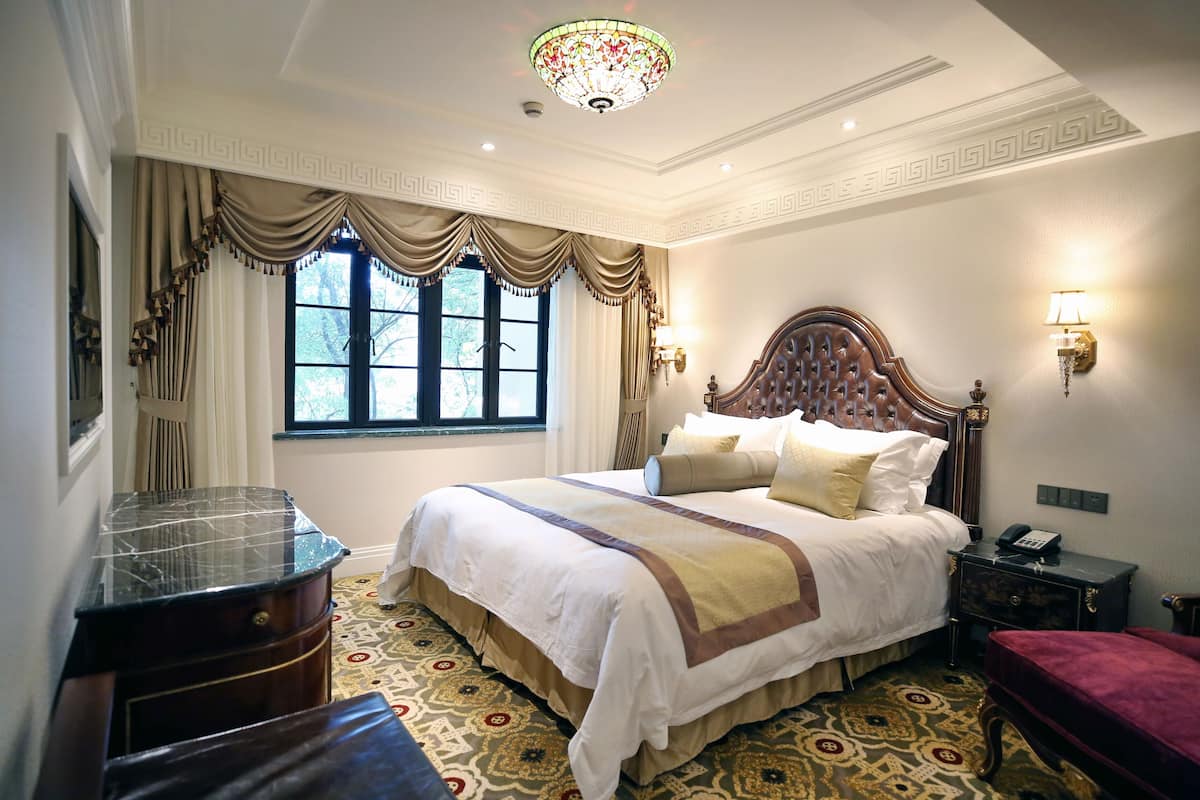 A hotel room with a large bed, a chandelier, a nightstand, and a patterned floor.