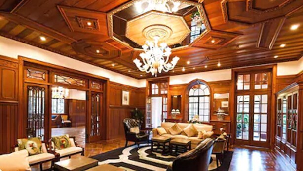 A spacious living room with a high ceiling, wooden paneling, and a chandelier. There are multiple seating areas with sofas and a coffee table. - Moller Villa Hotel Shanghai (Shanghai)