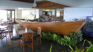 Ein Restaurant mit einer holzgetäfelten Theke in Bootsform, einem Sitzbereich mit Stühlen und Tischen sowie einem Kühlschrank für Pepsi.
