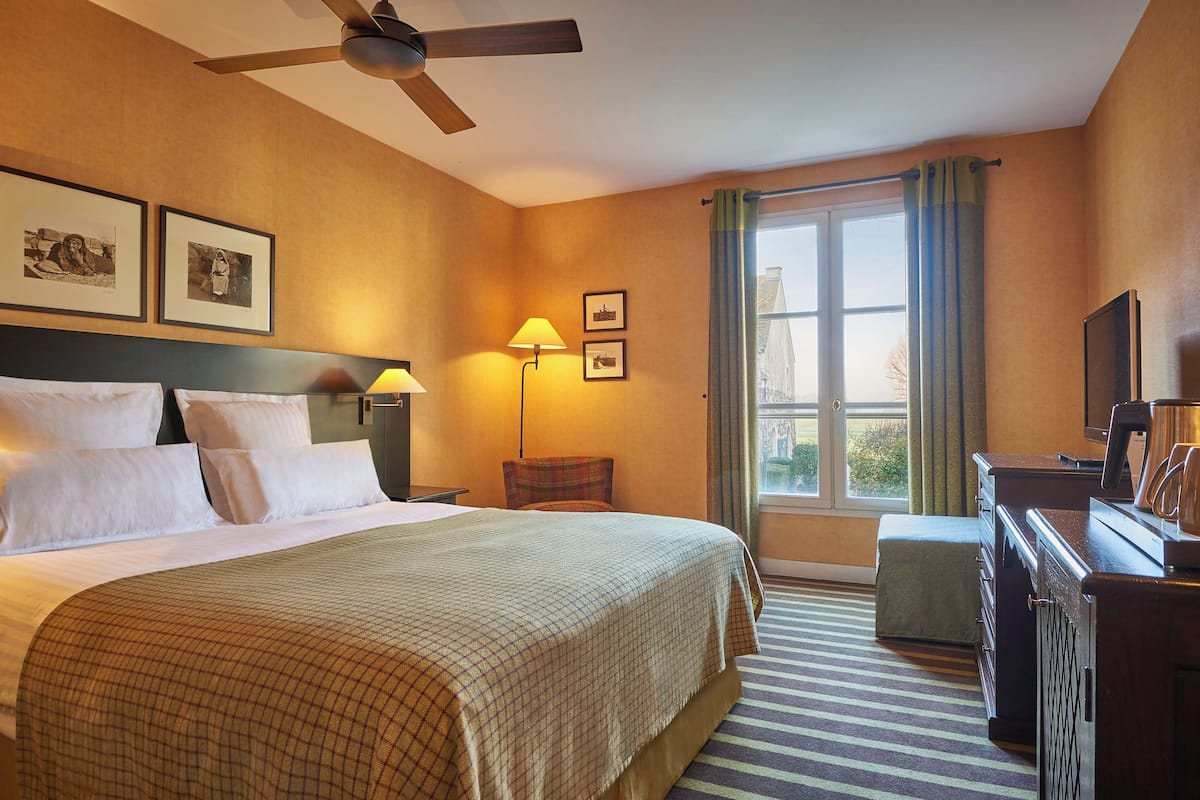 A hotel room with a bed, a desk, a chair, a lamp, and a television.