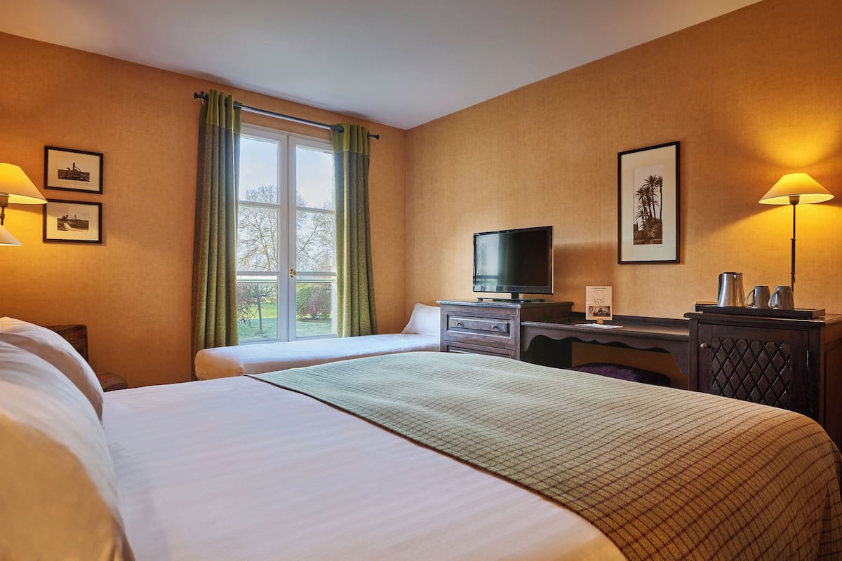 A hotel room with two beds, a television, a desk with a lamp, and framed pictures on the walls.