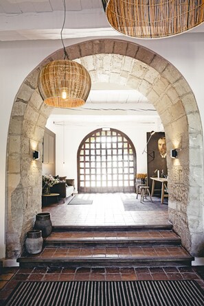 An arched doorway leading to a room with a large window, a table with chairs, and a hanging light fixture.