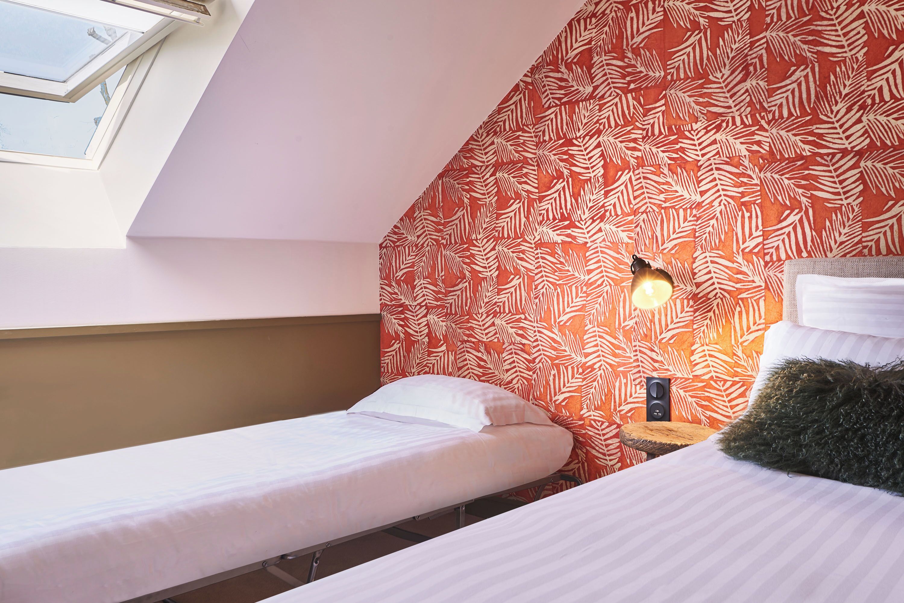 A room with two beds, a sloped ceiling, and a patterned wall.