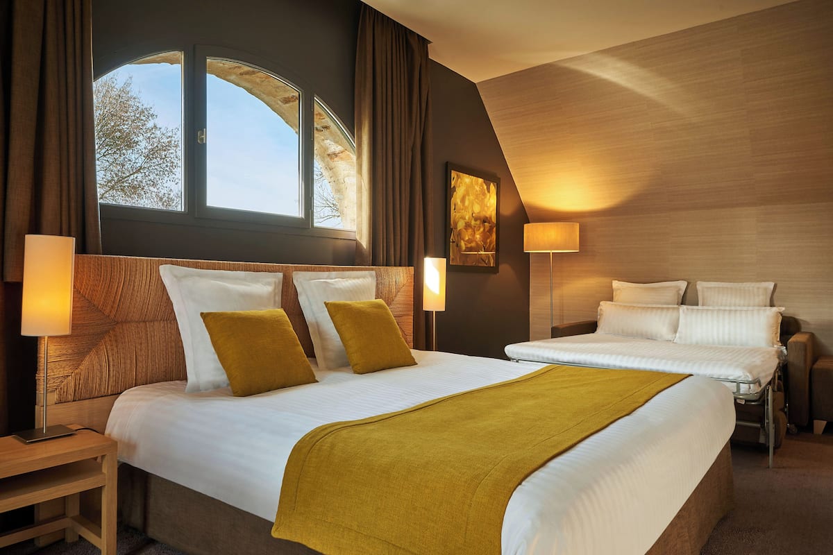 A hotel room with a large bed, a smaller bed, a desk, and a window with curtains.