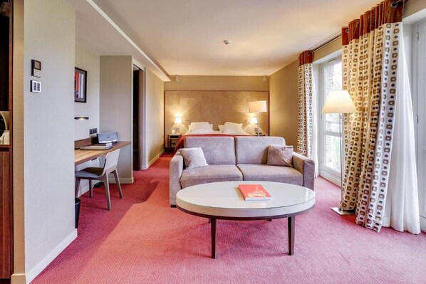 A hotel room with a bed, a sofa, a desk, and a round table.