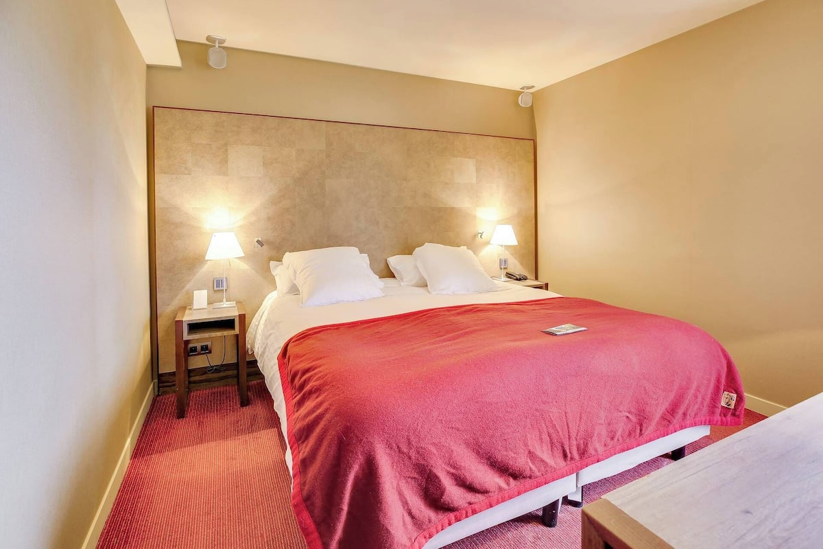 A hotel room with a bed, two bedside lamps, a telephone, and a red carpet.